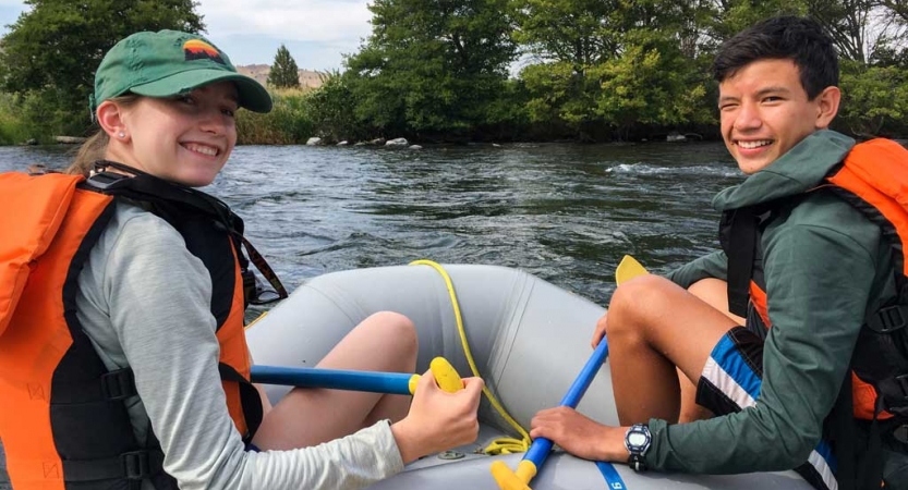 two young people sitting at the front of a raft look back at the camera and smile